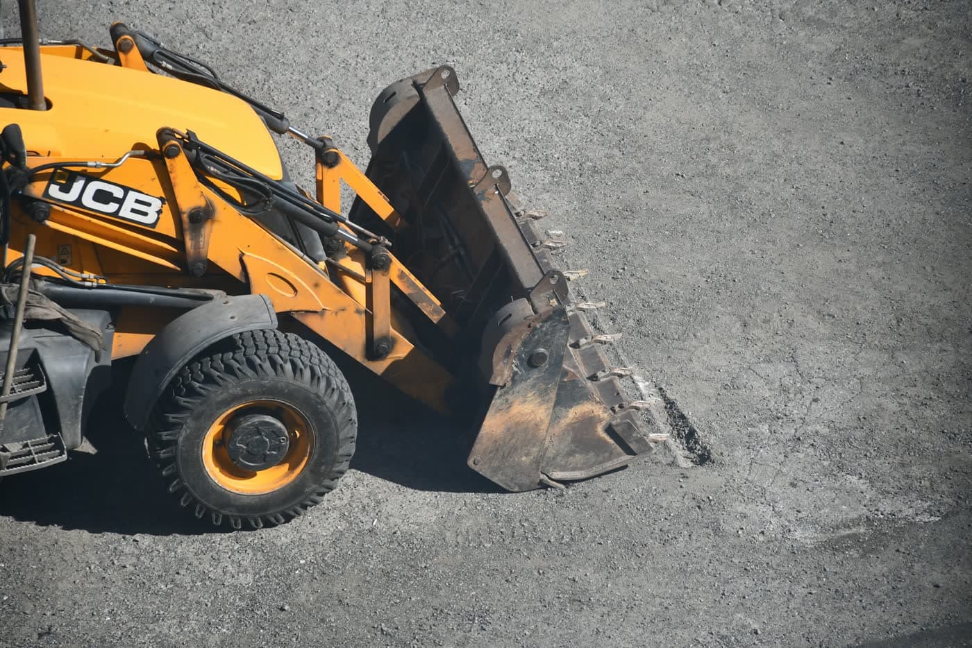 JCB backhoe loader with its front bucket lowered on gravel.