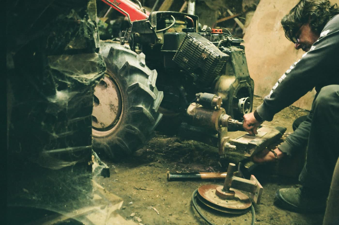 Mechanic repairing the engine of a walk-behind tractor in a barn.