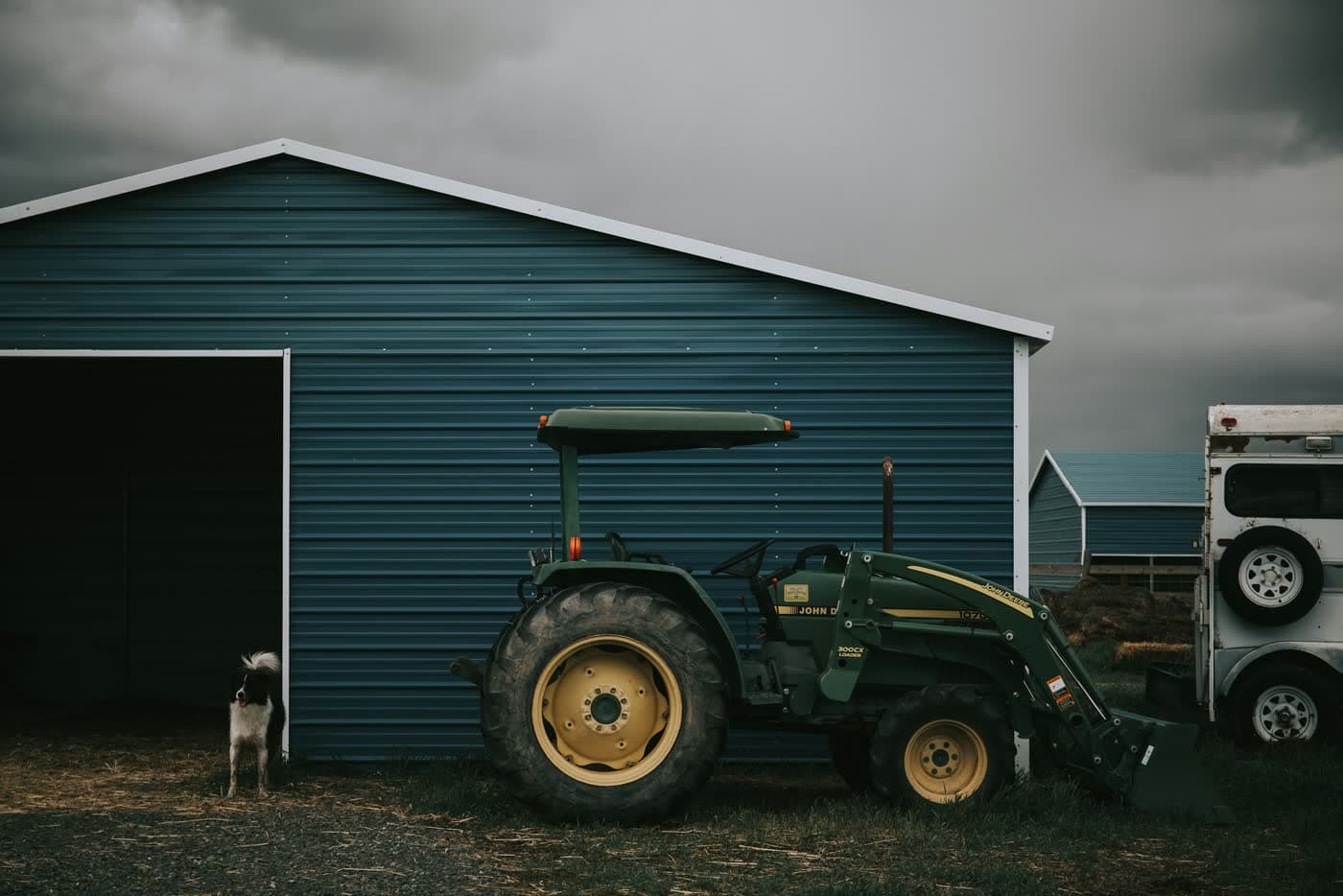 John Deere compact tractor with loader parked beside a farm shed.