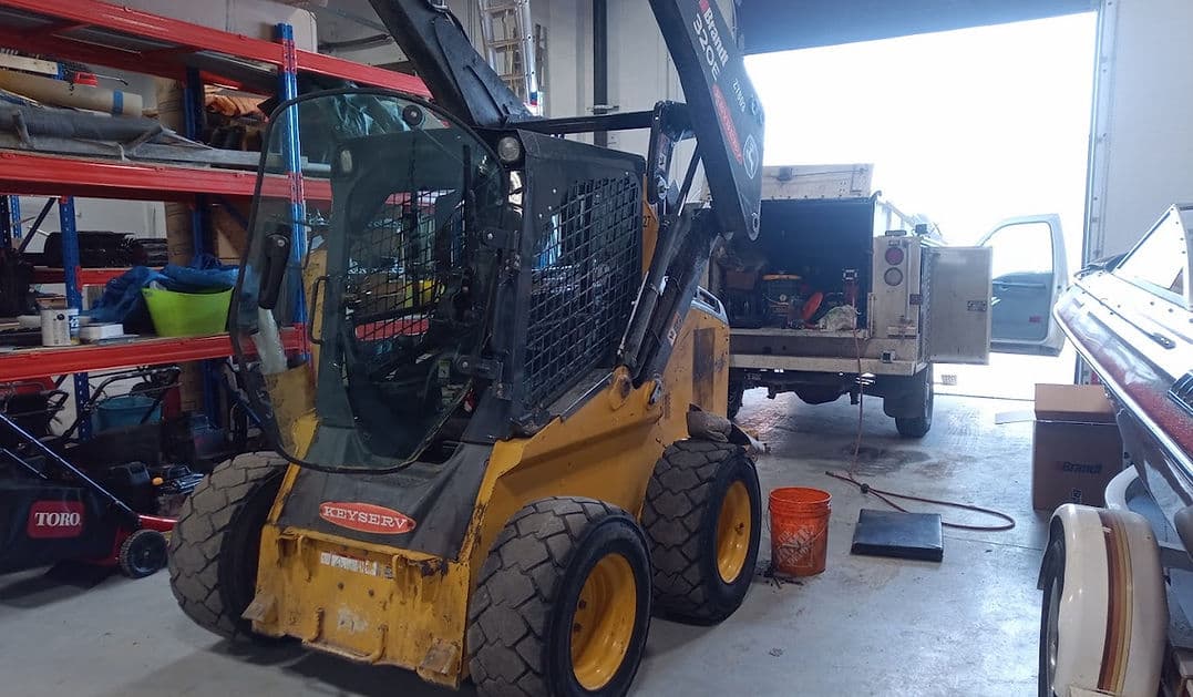 John Deere 320E skid steer with the boom raised for repair in the JSD shop.