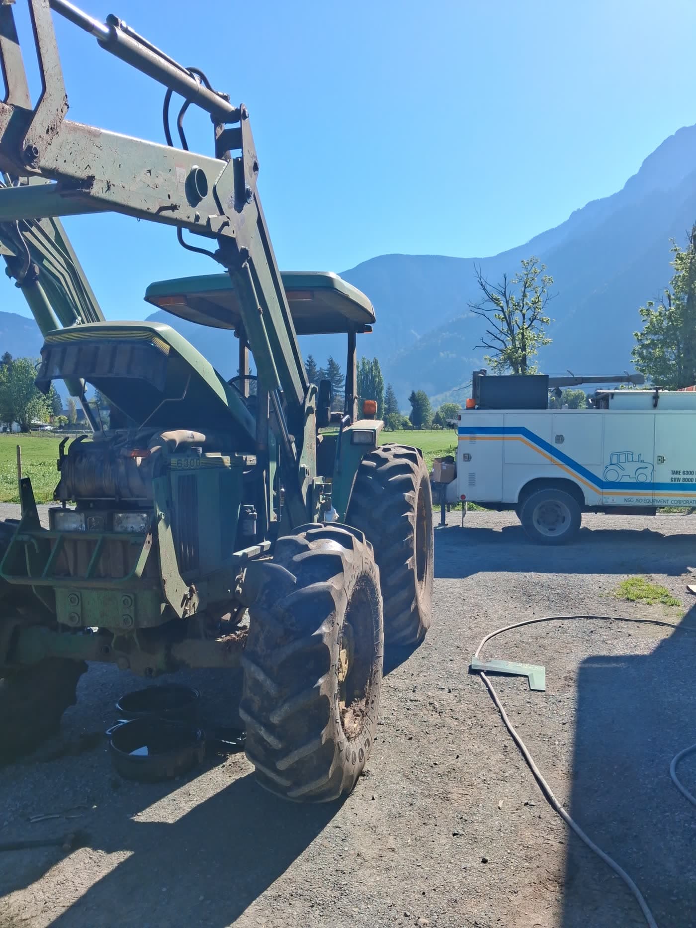 John Deere agricultural tractor working in a field alongside a combine, full-size ag tractors that JSD services on bigger Fraser Valley farms and dairy operations.