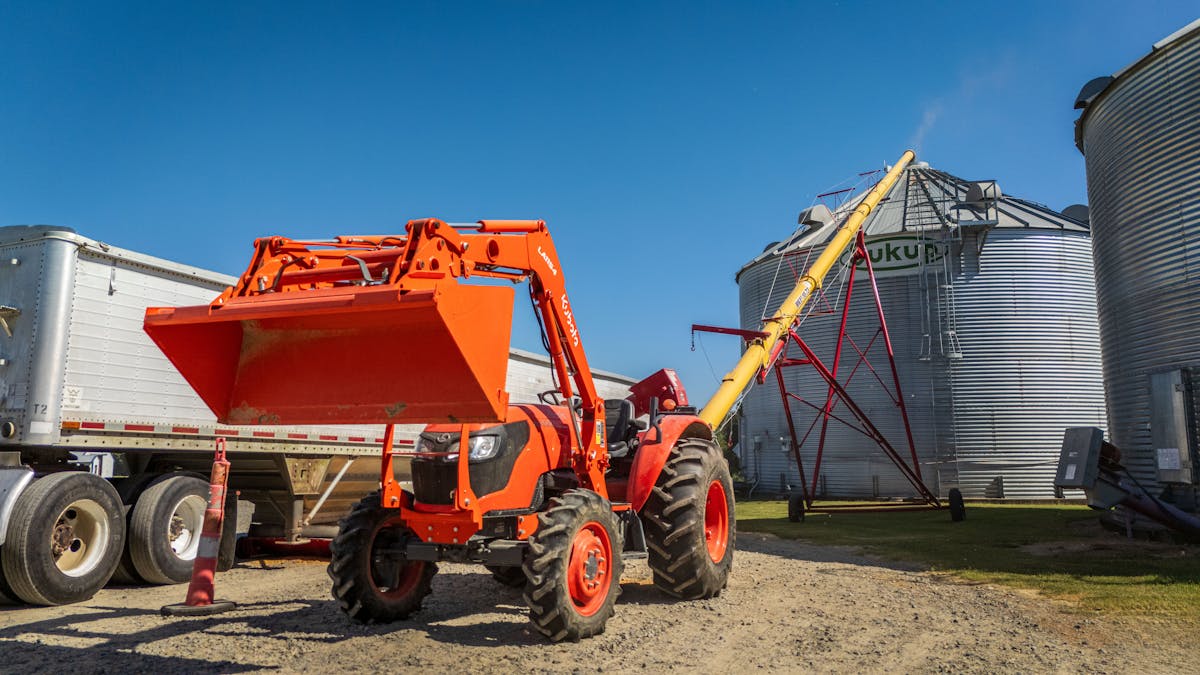 Kubota tractor with front-end loader working beside grain bins — Kubota equipment JSD services on-site.