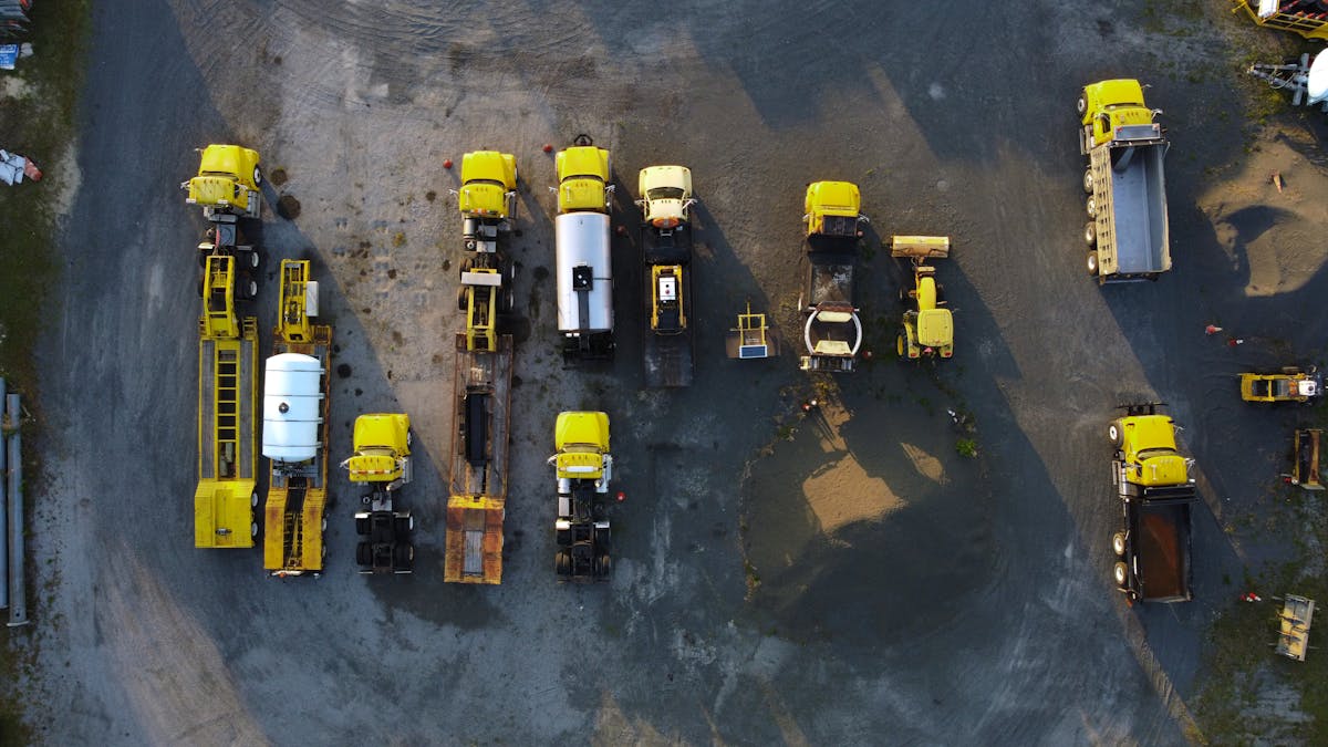 Aerial view of a fleet of yellow trucks and equipment staged in a gravel yard.