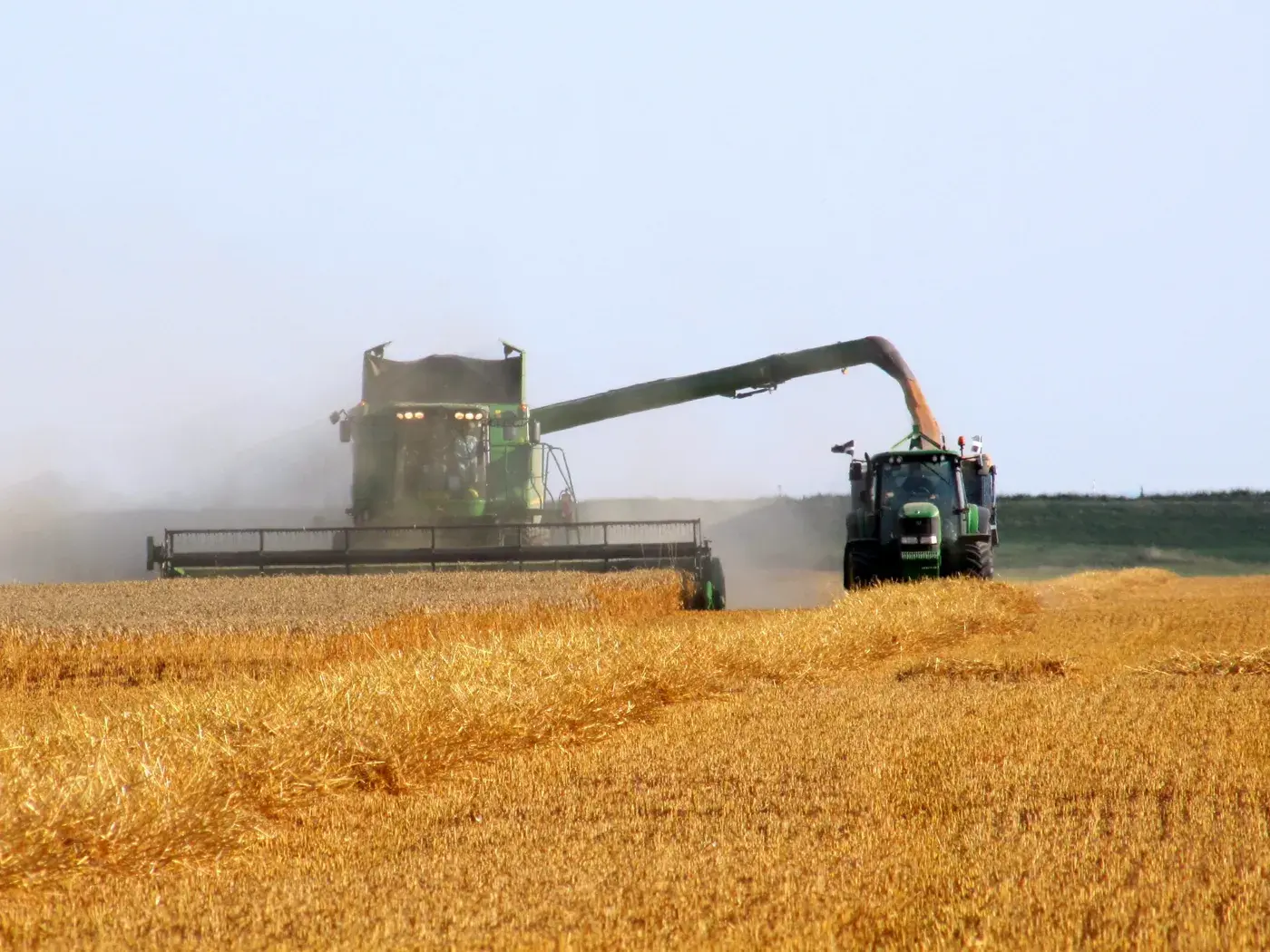John Deere combine unloading grain into a tractor-pulled grain cart at harvest.